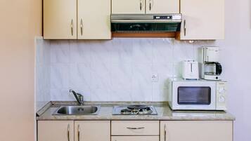 Una cocina compacta con microondas, tostadora y cafetera sobre la encimera, un fregadero y armarios con tiradores.