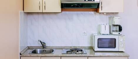 Una cocina compacta con microondas, tostadora y cafetera sobre la encimera, un fregadero y armarios con tiradores.