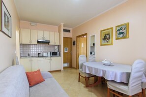 A compact living space with a kitchenette, a dining area with a table and chairs, and a sofa with a cushion.