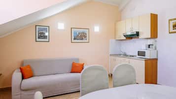 Un espacio habitable compacto con kitchenette, un sofá con cojines naranjas y dos cuadros en la pared.