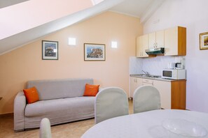 A compact living space with a kitchenette, a sofa with orange cushions, and two framed pictures on the wall.