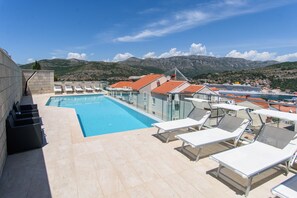 A rooftop pool area with lounge chairs and a view of a coastal town and mountains.