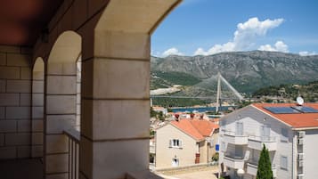 Un balcón con arcos de piedra con vistas a un pueblo costero, un puente atirantado y montañas al fondo.