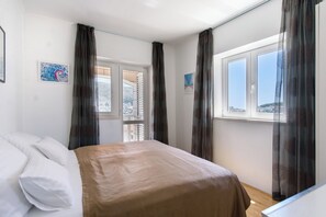 Quarto com cama, janela com cortinas e porta que dá para uma varanda externa.