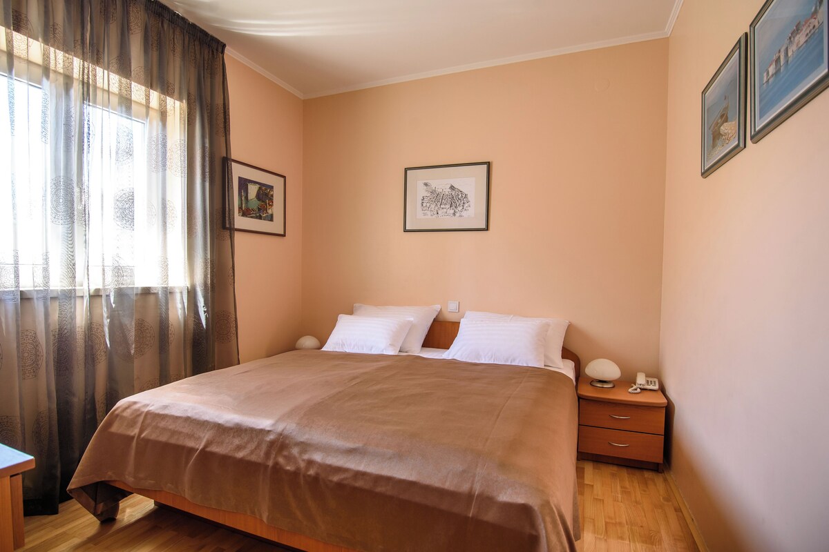 Um quarto com uma cama, uma mesa de cabeceira, um abajur e uma janela com cortinas.