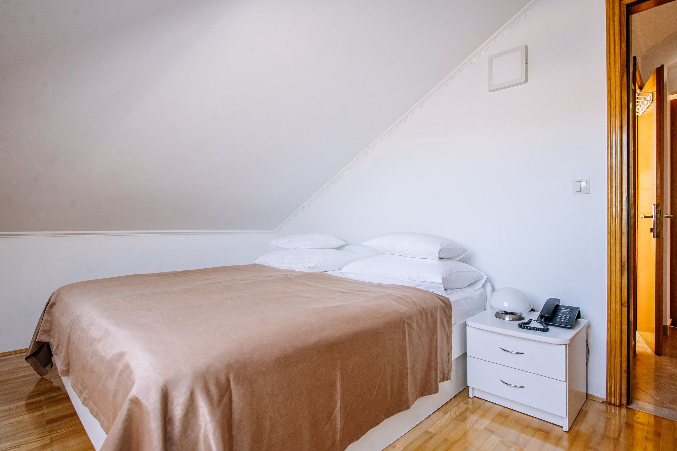Un dormitorio con cama, mesita de noche blanca y puerta de madera.