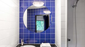 Un baño moderno con un espejo redondo, un lavamanos y una ducha.