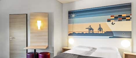 Habitación de hotel con cama, dos mesitas de noche, una lámpara de pared, un adorno en la pared y una puerta.