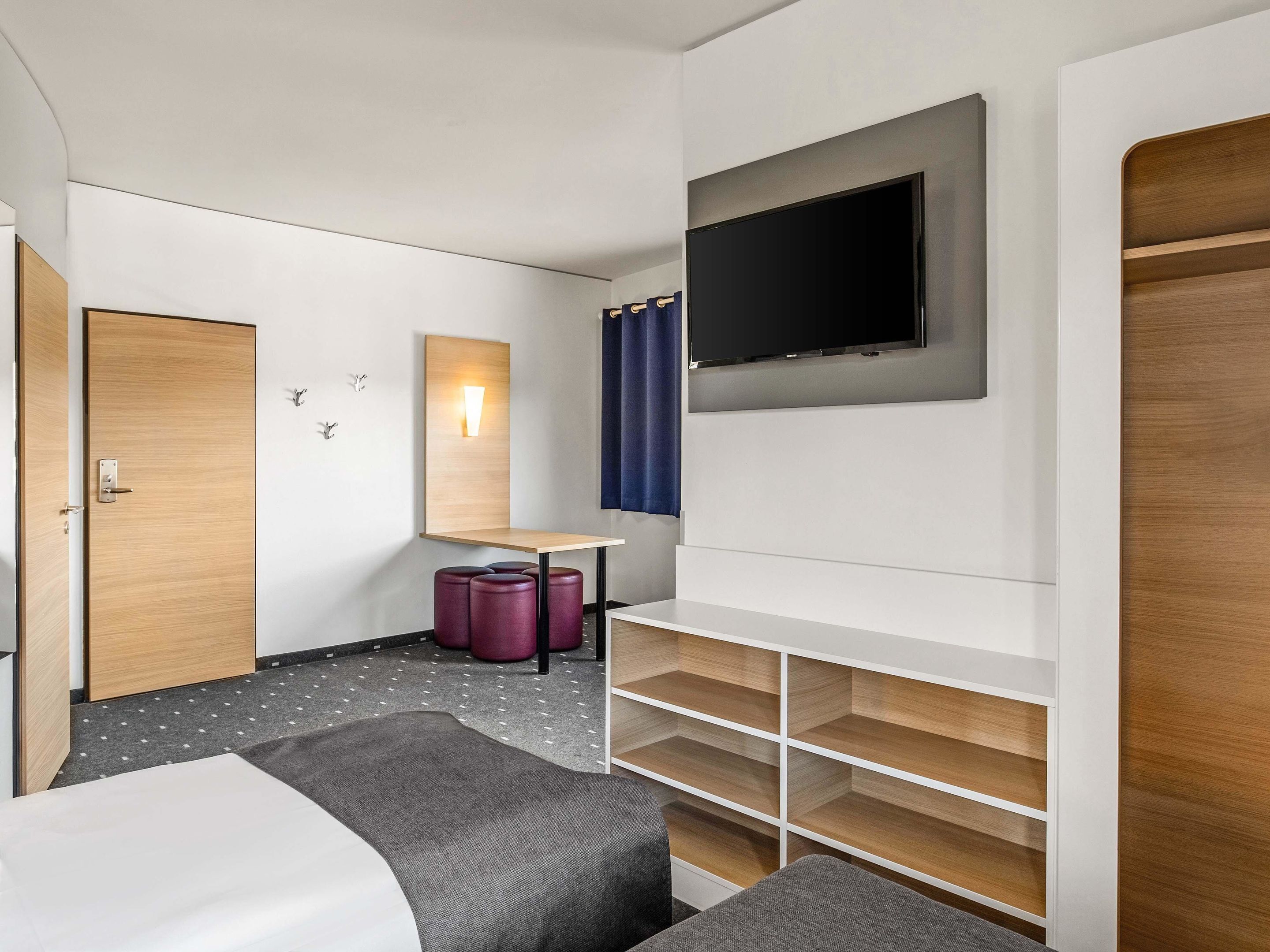 Ein Hotelzimmer mit Bett, Schreibtisch, Fernseher und Kleiderschrank.
