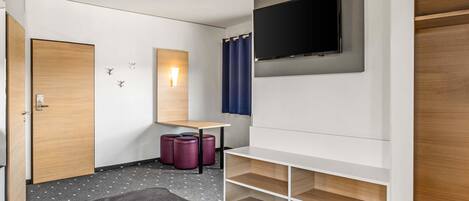 Una habitación de hotel con una cama, un escritorio, un televisor y un armario.