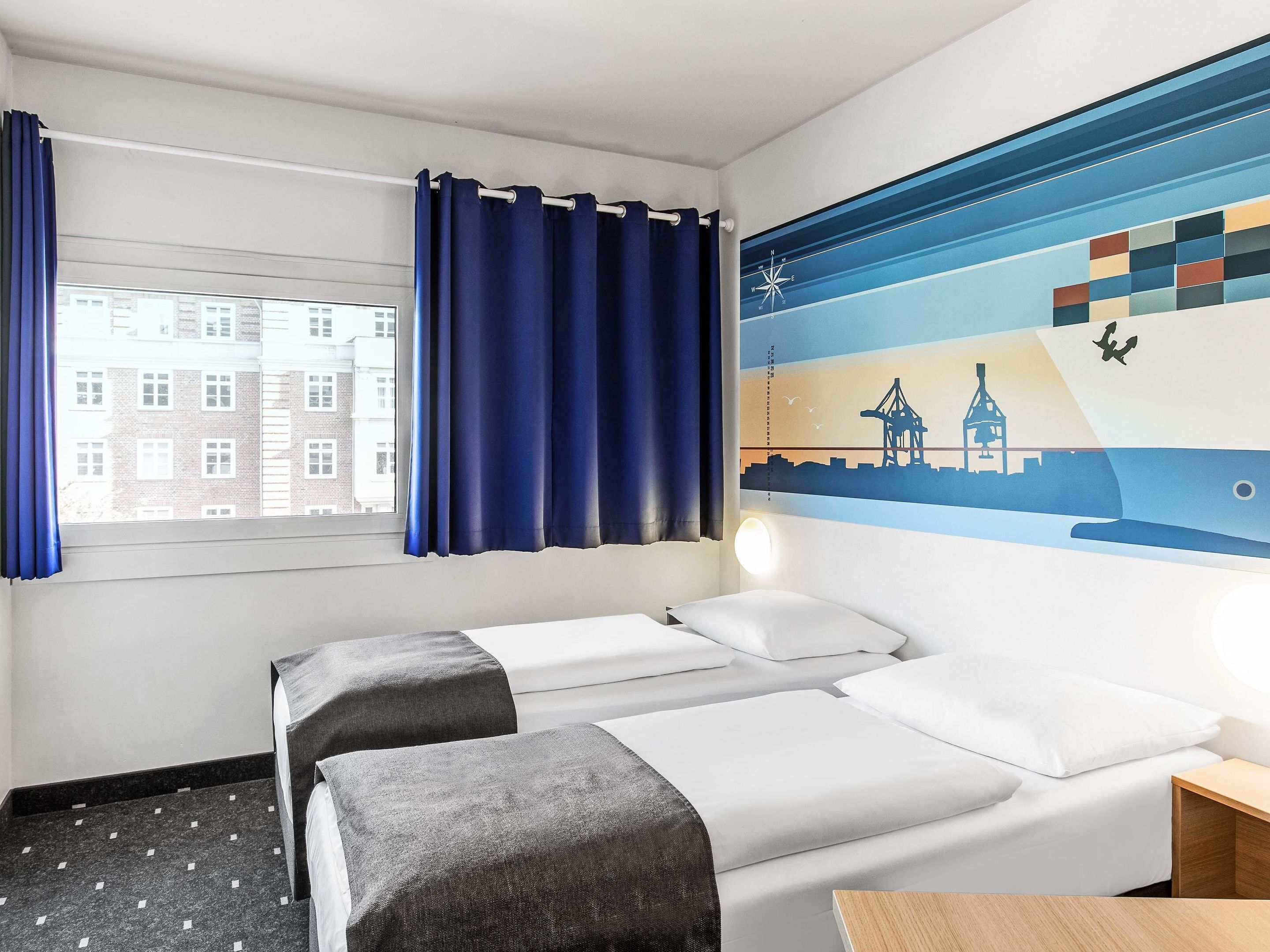 Ein Hotelzimmer mit zwei Betten, einem Fenster mit Vorhängen, einem Wandbild und einem Nachttisch.