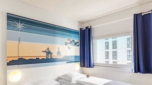 Habitación de hotel con dos camas, una obra de arte en la pared que muestra un paisaje urbano, una ventana con cortinas y una mesita de noche.