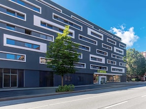 Een modern hotelgebouw met een platte gevel, meerdere ramen en een bord waarop staat dat het een B&B is.