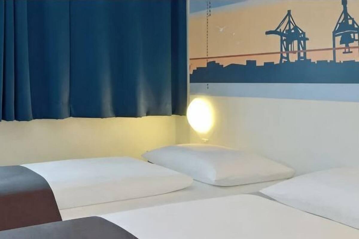 Une chambre d’hôtel avec un lit, des oreillers, une lampe fixée au mur et une fresque représentant des grues.