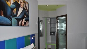 Ein Hotelzimmer mit einem Bett, einem Kleiderschrank, einem grünen Sessel und einem Bild an der Wand.