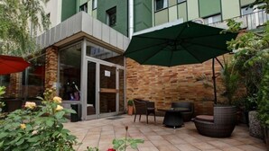 Eine Außenpatio-Terrasse mit einer Ziegelwand, einem Glastür-Eingang und Sitzgelegenheiten inklusive Tisch und Stühlen.