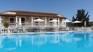 A swimming pool with lounge chairs and umbrellas, a building with a tiled roof, and a white fence.