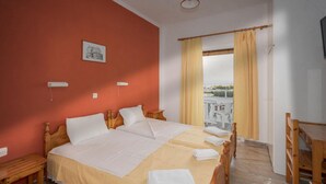 A double bed with white linens, a wooden headboard, and a view of the sea through a window with yellow curtains.