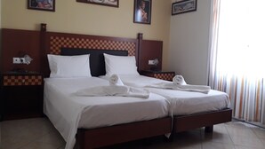 A hotel room with a checkered headboard, two white beds, and towels neatly folded on each bed. - Parthenon (Ios)