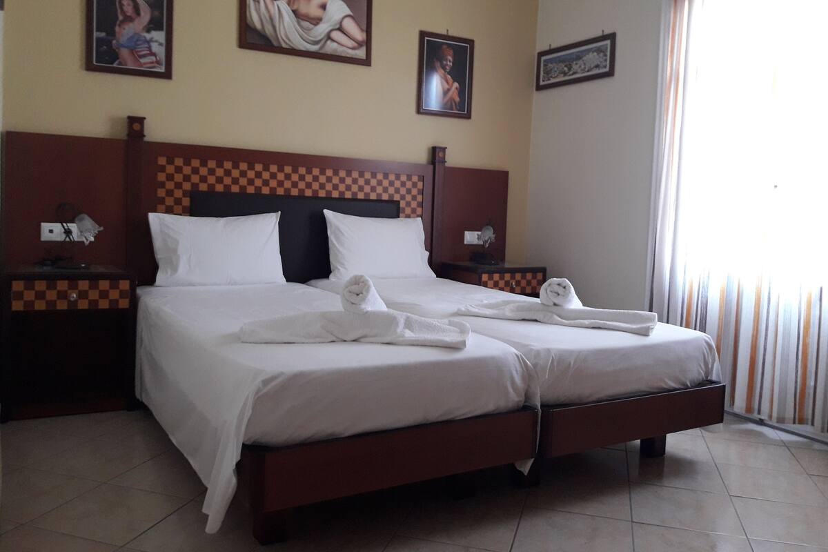 Quarto de hotel com cabeceira xadrez, duas camas brancas e toalhas dobradas em cada cama.