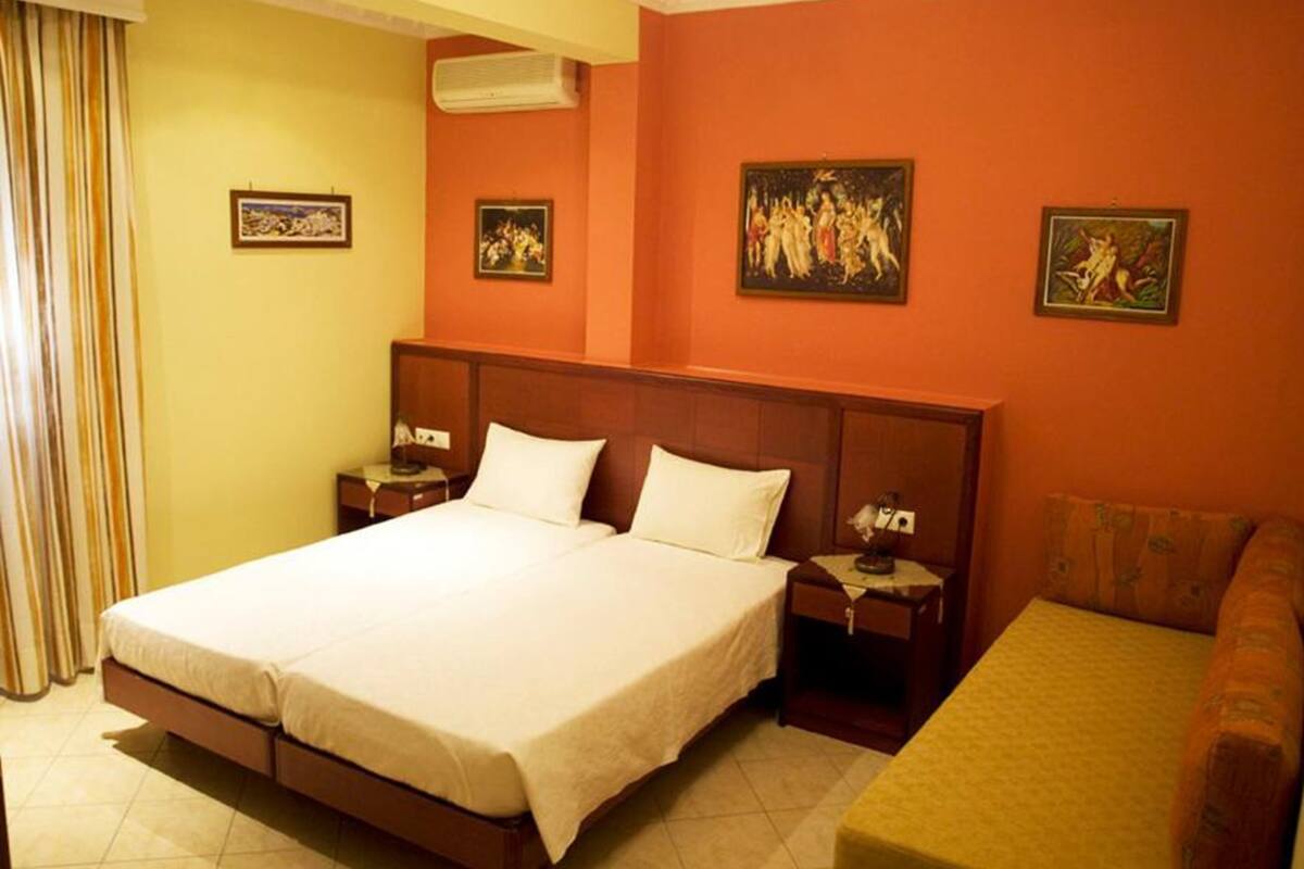Quarto de hotel com uma cama de casal, duas mesas de cabeceira, um sofá e três obras de arte emolduradas nas paredes.