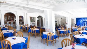 A spacious dining area with multiple tables and chairs, white walls, and blue tablecloths. - Parthenon (Ios)
