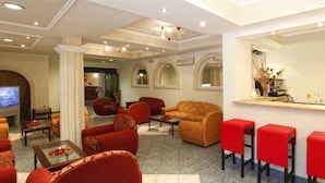 A hotel lobby with red sofas, a coffee table, a TV, and a bar area with red stools. - Hotel Galaxias (Corfu)