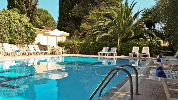 A swimming pool with lounge chairs and umbrellas, surrounded by trees and greenery. - Hotel Galaxias (Corfu)