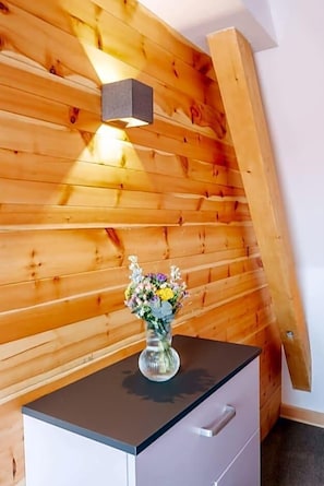 A wooden wall with a light fixture and a vase of flowers on a cabinet.