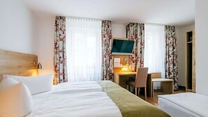 Une chambre d’hôtel avec un lit, un bureau, une chaise, une télévision et des rideaux.