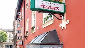 Hotel Andres, con facciata rossa, insegna raffigurante una carrozza trainata da cavalli e tenda da sole verde.