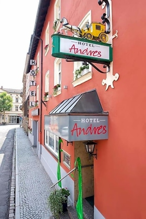 A hotel named 'Andres' with a red facade, a signboard with a horse and carriage, and a green awning.