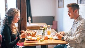 Une table à manger avec de la nourriture et des boissons, un vase rempli de fleurs et une fenêtre en arrière-plan.