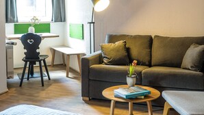 A cozy room with a wooden ceiling, a sofa, a desk, a chair, and a bed. - Das Nordberg Guesthouse (Garmisch-Partenkirchen)