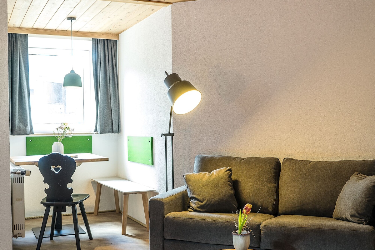 A cozy room with a wooden ceiling, a sofa, a desk, a chair, and a bed.