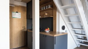 A compact kitchen with a wooden countertop, a bowl of fruit, and a white staircase. - Das Nordberg Guesthouse (Garmisch-Partenkirchen)