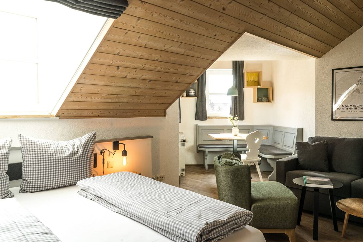 A cozy room with a bed, a green armchair, a small table, and a bench.