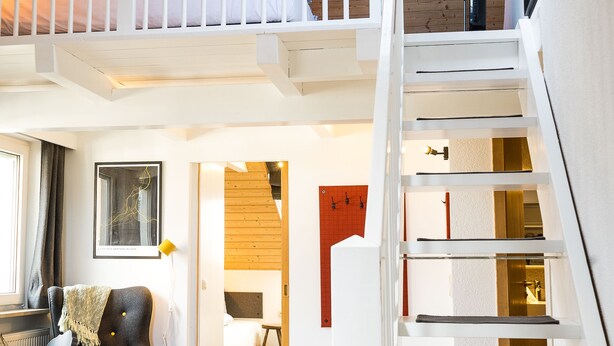A loft-style bedroom with a white staircase, wooden beams, and a view of the living area below. - Das Nordberg Guesthouse (Garmisch-Partenkirchen)
