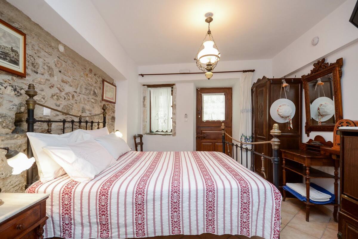 A bedroom with a bed, wooden furniture, a stone wall, and a chandelier.