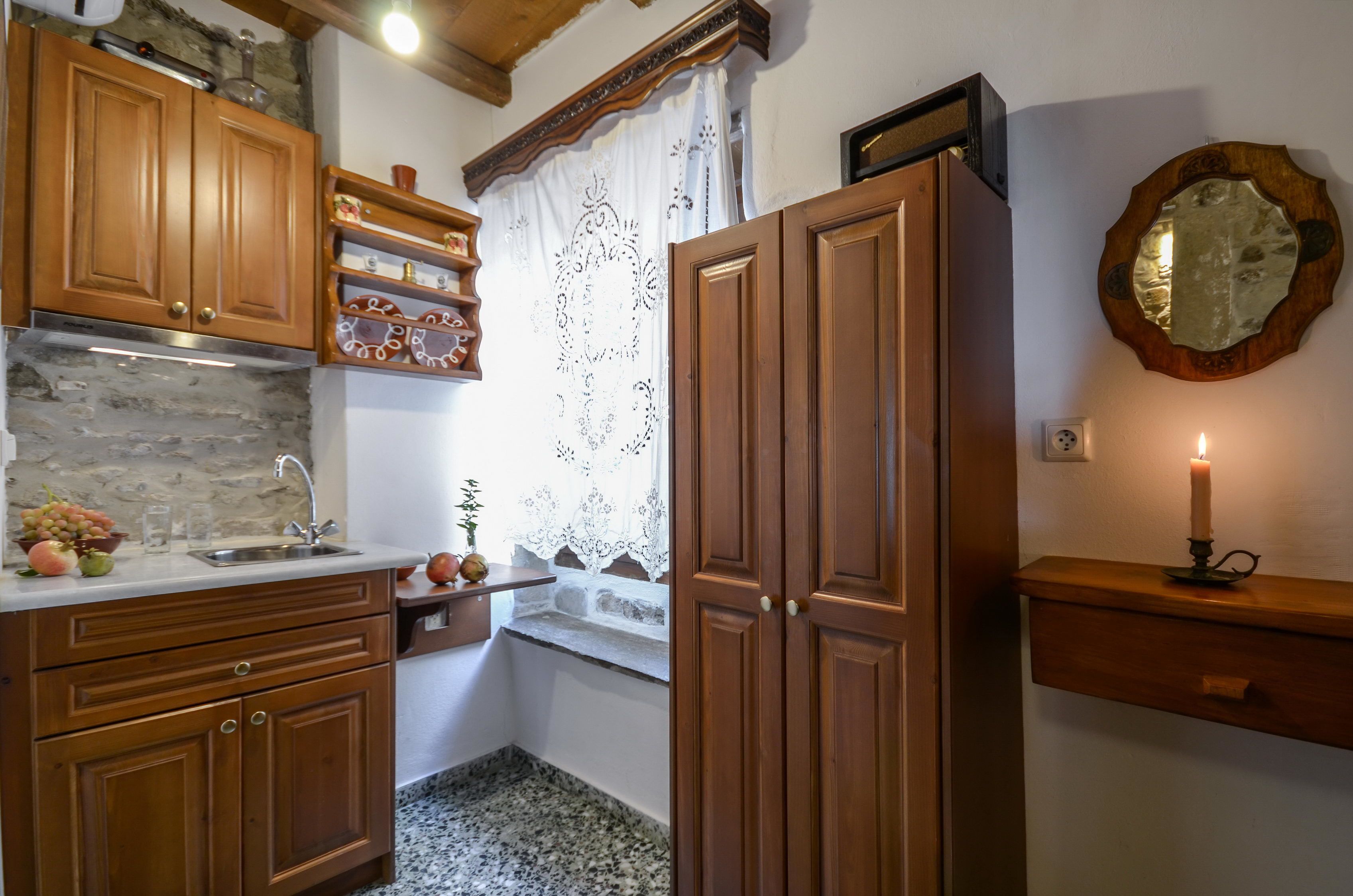 Una cocina con armarios de madera, salpicadero de piedra, una ventana con cortinas de encaje y una vela en un estante.