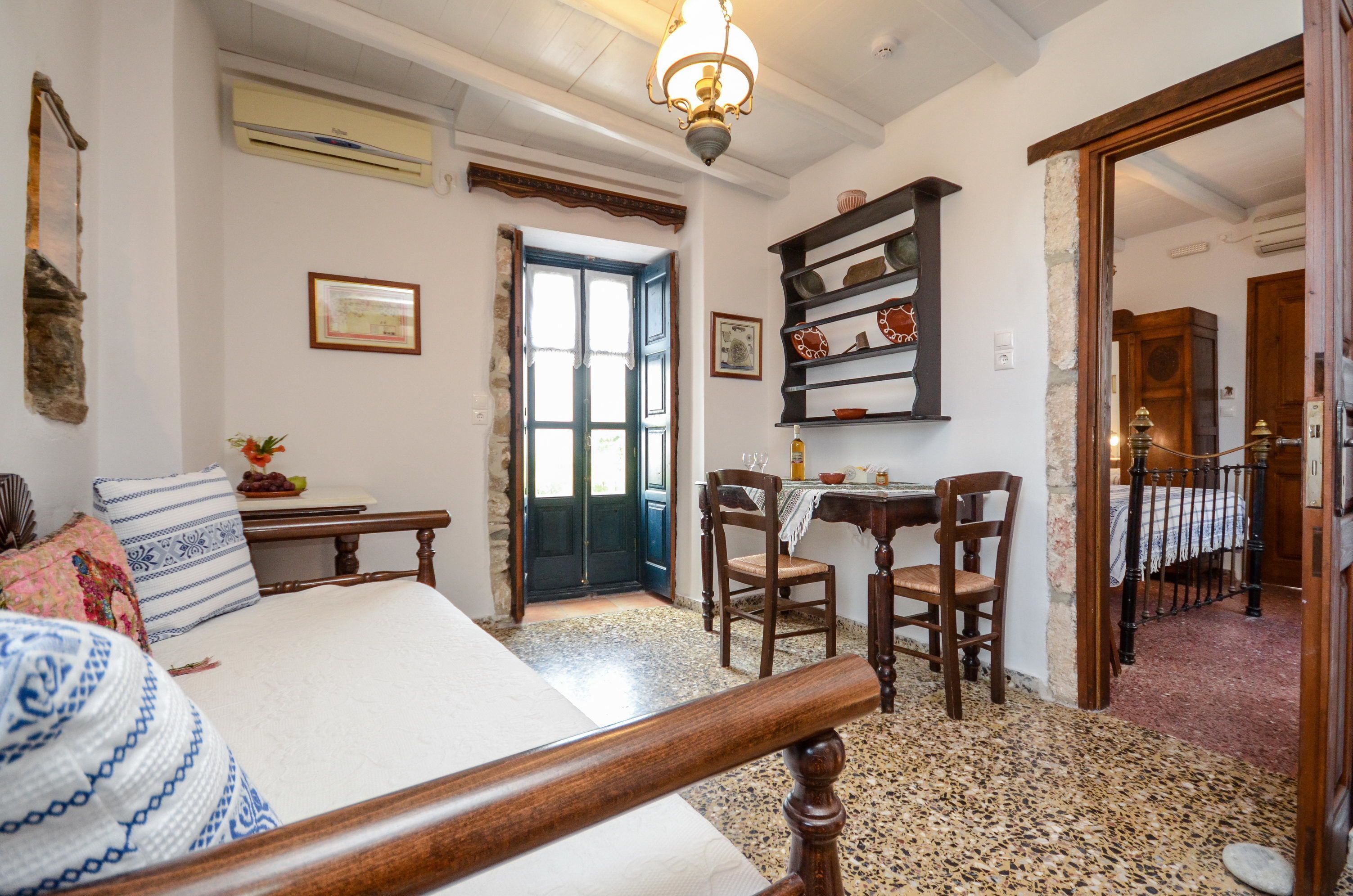 A bedroom with a bed, a desk, chairs, a bookshelf, and a door leading to another room.