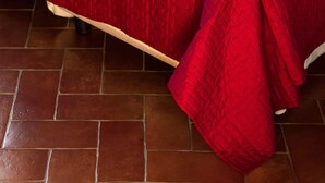 A neatly made bed with a red quilt, white linens, and a folded towel. - Casa Calicantus (Milan)