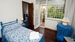 A bedroom with a bed, a bedside table with a lamp, a window with a view of greenery, and a door leading to a bathroom. - 2 Passi Da (Rome)