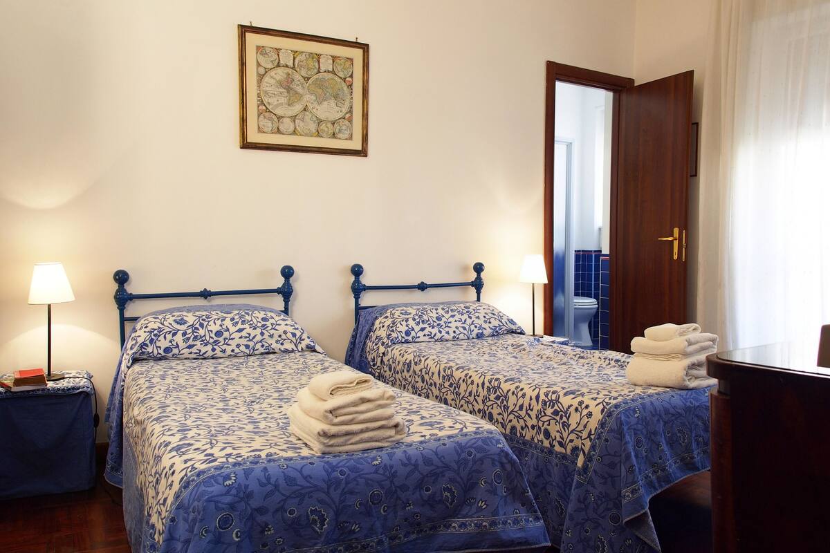 A hotel room with two beds, a map on the wall, a bathroom visible through an open door, and a desk with a chair.