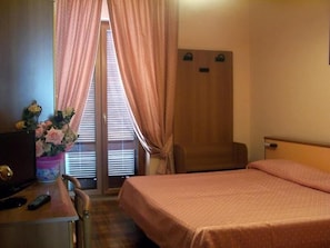 A hotel room with a bed, a desk with a lamp, a chair, a window with curtains, and a door. - Hotel Belvedere (Caserta)