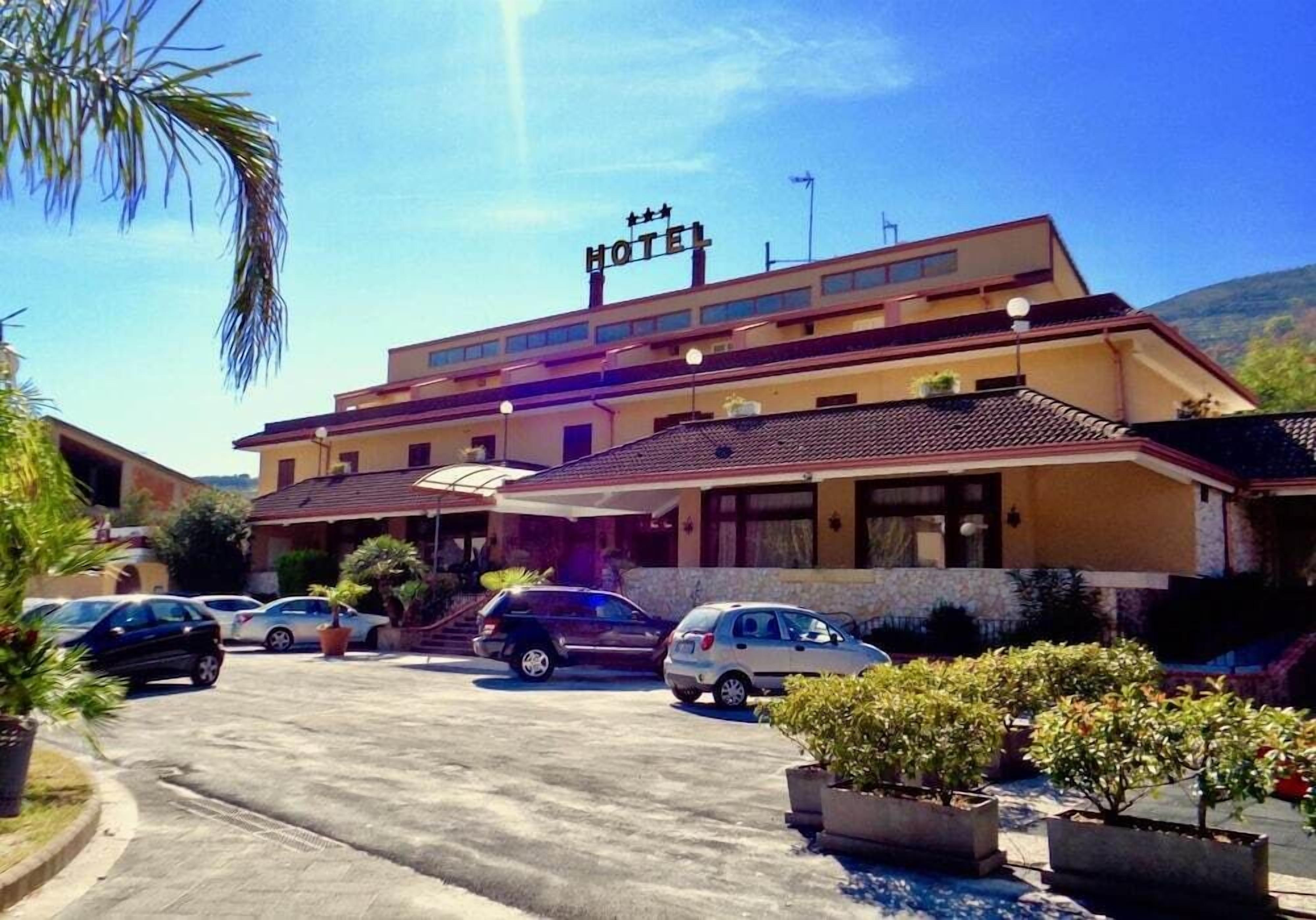 A hotel with a prominent "HOTEL" sign, a covered entrance, and a parking lot with several cars.