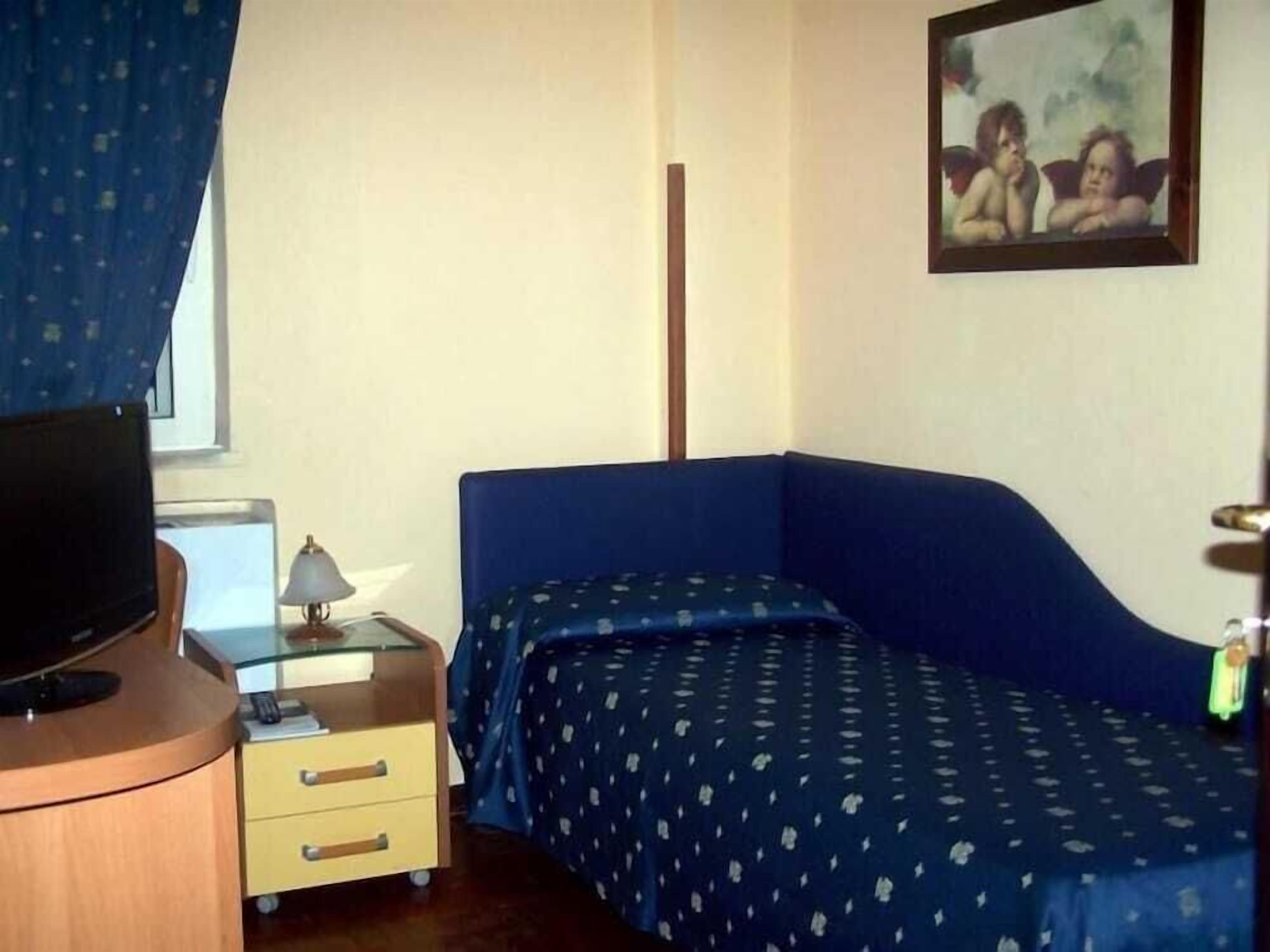 Ein Schlafzimmer mit einem Einzelbett, einem kleinen Nachttisch mit Lampe, einem Fernseher auf einem Schrank und einem Bild an der Wand.
