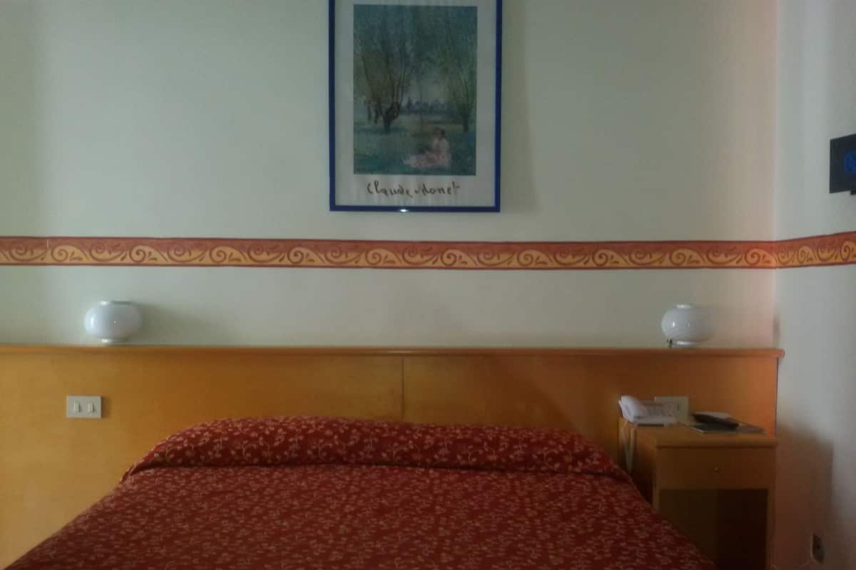 A hotel room with a bed, a nightstand, a lamp, and a framed picture on the wall.