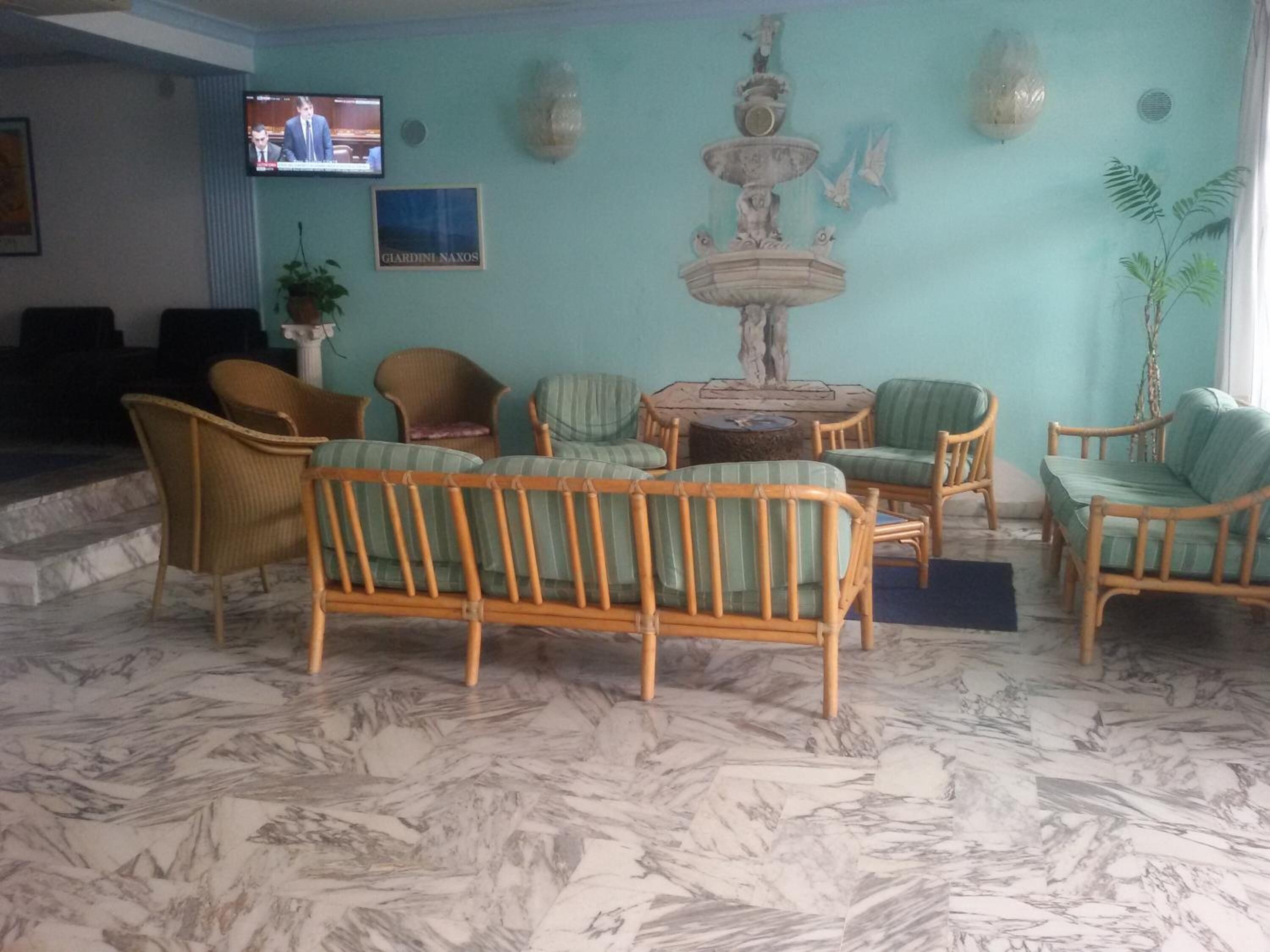 Un hall d’entrée avec un sol en marbre, des meubles en osier, une fontaine et un écran de télévision.
