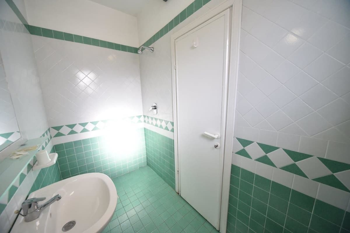 A bathroom with a sink, a door, and green and white tiled walls.